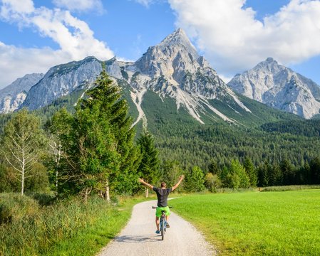 Cyclist with mountain bike rides hands-free, with raised arms, on the cycle path Via Claudia Augusta, crossing the Alps, at the back Sonnenspitze, mountain landscape, Tyrolean Alps, crossing the Alps, at Ehrwald, Tyrol, Austria, Europe