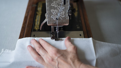 Sewing process. Foot of old vintage sewing machine and hands of elderly woman. Selective focus