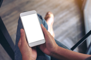 Top view mockup image of a woman holding white smart phone with blank desktop screen while sitting in cafe