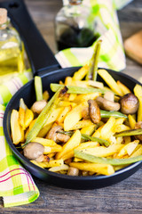 fried potatoes with mushrooms and asparagus in a pan on a wooden board