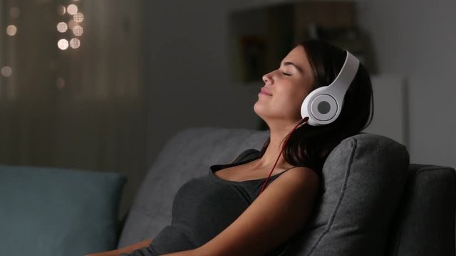 Girl relaxing listening to music sitting on a couch in the night at home