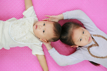 Obraz na płótnie Canvas Adorable cute Asian sister and little brother lying on pink mattress mat looking at camera. View from above.