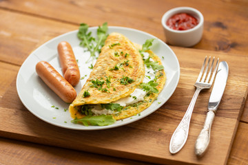 Omelette with herbs, soft cheese, grilled sausages and tomato sauce. Delicious breakfast