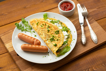 Omelette with herbs, soft cheese, grilled sausages and tomato sauce. Delicious breakfast