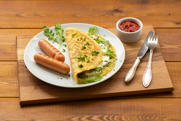 Omelette with herbs, soft cheese, grilled sausages and tomato sauce. Delicious breakfast
