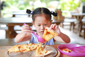 Little child girl enjoy eating pizza on the table.