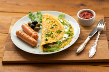 Omelette with herbs, soft cheese, grilled sausages, olives and spicy tomato sauce. Delicious breakfast