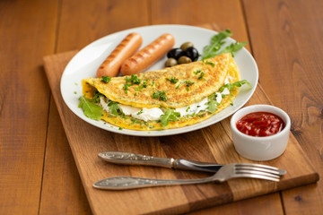 Omelette with herbs, soft cheese, grilled sausages, olives and spicy tomato sauce. Delicious breakfast