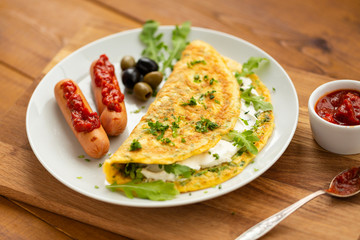 Omelette with herbs, soft cheese, grilled sausages, olives and spicy tomato sauce. Delicious breakfast