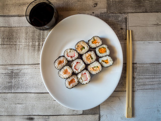 Roll of sushi prepared from raw fish and a special rice on white plate with chopsticks and sauce