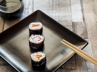 Simple roll of sushi prepared from raw fish and a special rice on black plate with chopsticks 