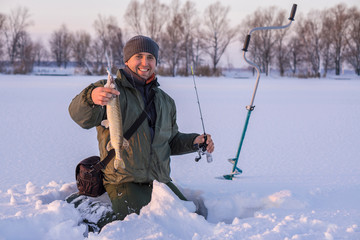 Fototapeta na wymiar Winter fishing concept. Fisherman in action with trophy in hand. Catching pike fish from snowy ice at lake.