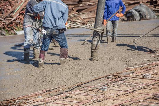 Workers using a wooden spatula for cement after Pouring ready-mixed concrete on steel reinforcement to make the road by mixing mobile the concrete mixer.