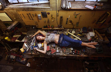 A young beautiful woman finds time to sleep during  her working hours. She lies down on the work bench filled with tools and other electronic devices. - Powered by Adobe