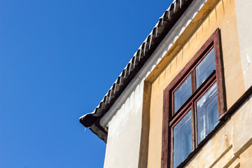 Wintry roof of the house with icicles on blue sky background