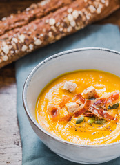 Pumpkin cream soup bowl.Roasted pumpkin soup with pumpkin seeds and crispy bacon on wooden background.