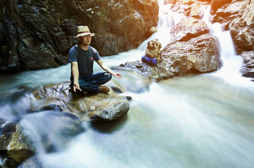 male hiker doing yoga on rock near waterfall