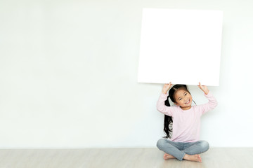 Young little asian girl or kid enjoy holding empty white placard board for media banner, business content presentation, mock up blank sign for message with positive and fun in creative design concept.
