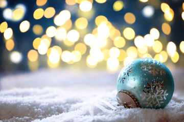 blaue Weihnachtskugel im Schnee vor funkelndem Hintergrund
