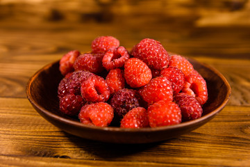 Ceramic plate with ripe raspberries on wooden table