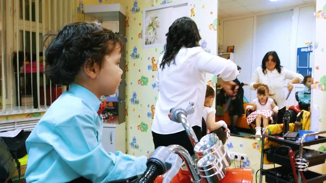 Children barbershop. Funny kid in hairdressing salon. Little boy sitting in toy motorcycle
