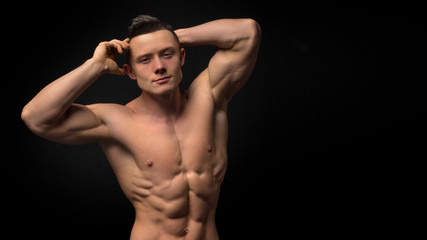 Fototapeta premium Portrait of strong healthy handsome Athletic Man Fitness Model posing near dark gray wall.