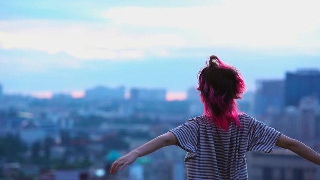Pink haired girl enjoys freedom and wind, roof top of city building, peace life