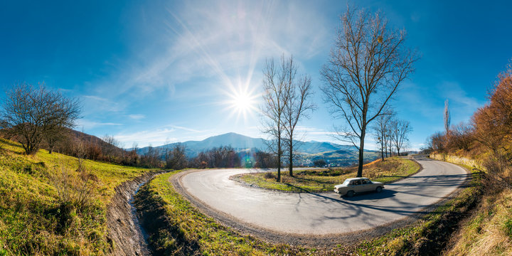 panorama of winding serpentine road. lovely autumn afternoon with bright sun on a blue sky. leafless trees by the road. village in valley and ridge in the distance. fast moving car uphill