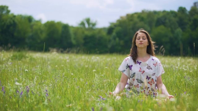 Woman sits in lotus pose meditating outdoors, wind moves hair, oneness nature