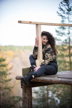 Young woman sitting on a platform on a background of the forest, smiling, hugging a rail