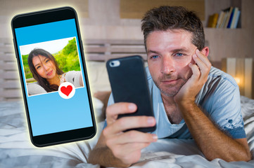 young handsome and happy man using internet social media on mobile phone searching love flirting and dating online sending like to beautiful Asian Chinese woman