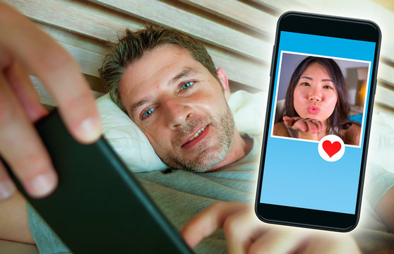 young handsome and happy man using internet social media on mobile phone searching love flirting and dating online sending like to beautiful Asian Chinese woman