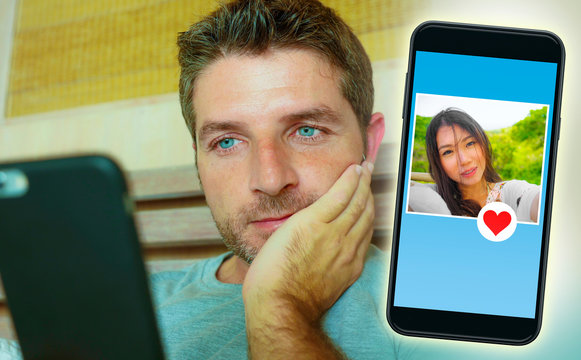 young handsome and happy man using internet social media on mobile phone searching love flirting and dating online sending like to beautiful Asian Chinese woman