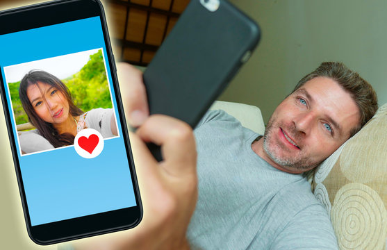 young handsome and happy man using internet social media on mobile phone searching love flirting and dating online sending like to beautiful Asian Chinese woman