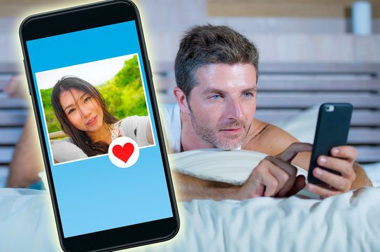 young handsome and happy man using internet social media on mobile phone searching love flirting and dating online sending like to beautiful Asian Chinese woman