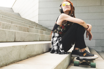 young girl with tattoo and dreadlocks listening to music while sitting on the steps