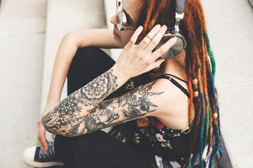 young girl with tattoo and dreadlocks listening to music while sitting on the steps