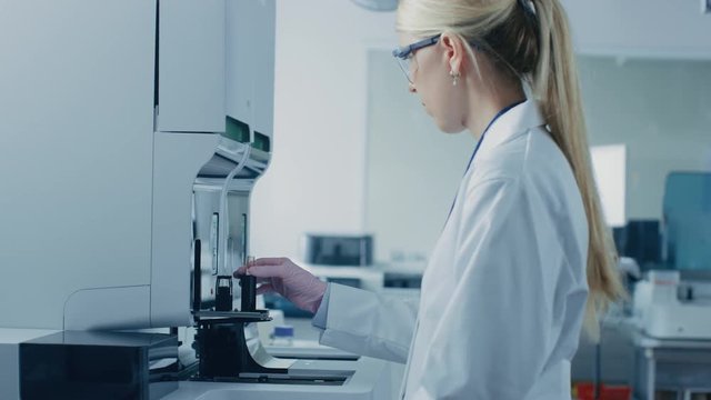 Female Research Scientist Takes Test Tube with Blood Sample and Places it Into Medical Analyzing Equipment. Scientist Works in Modern Pharmaceutical Laboratory