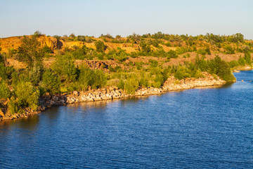 Summer sunset at the pond. Rocky coast with green trees