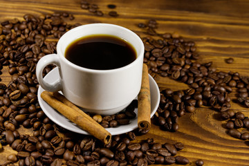 Cup of coffee, roasted coffee beans and cinnamon sticks on wooden table