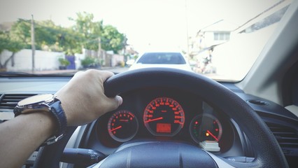 Steering wheel with driver hand on it in  car with view of street and another car nearly,...