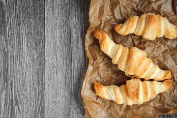 Four croissants on a wooden light cutting board on a wooden tabletop.