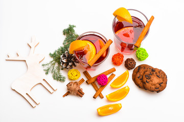 Glasses with mulled wine or hot drink near wooden deer decoration on white background, close up. Winter hot drinks concept. Mulled wine or hot beverage with cinnamon sticks, orange fruit and fir cone