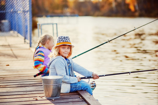 Two little girls fishing on the lake on a sunny morning.