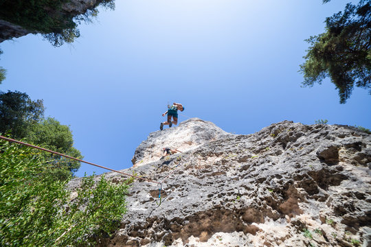 Young man climbing down the mountain doing rappel a sunny day 