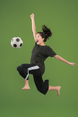 Forward to the victory.The young woman as soccer football player jumping and holding the ball at studio on green background. Football fan and world championship concept. Human emotions concepts