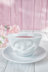 Pink tea in white cup and pink carnation flowers on a white background. Free space