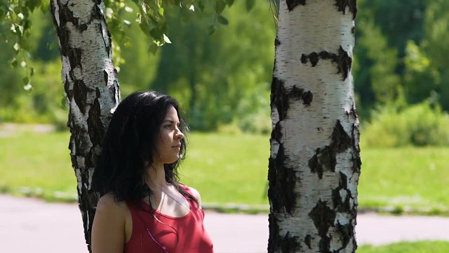 Woman in red dress standing under birch tree in park waiting for date partner