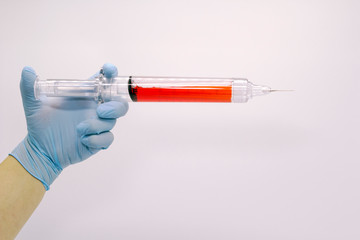 The surgeon's hand in a blue medical glove holds a large syringe with blood . Isolated background.