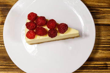 Piece of tasty New York cheesecake with raspberries in a white plate on wooden table. Top view
